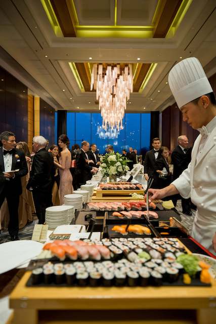 Sushi Wedding Food Station Live sushi chef at wedding reception buffet with assorted rolls and nigiri guests mingling in ballroom