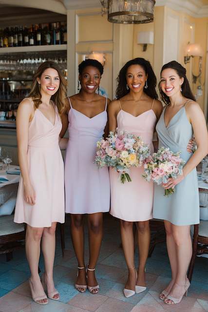 Bridesmaids in dress with Spring Summer colors Bridesmaids in soft pastel dresses, smiling and holding vibrant floral bouquets at a rehearsal dinner