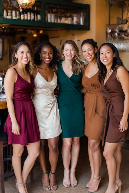 Bridesmaids in dress with fall and winter colors Bridesmaids smiling and posing together, each in a different rich, warm-colored dress at a rehearsal dinner