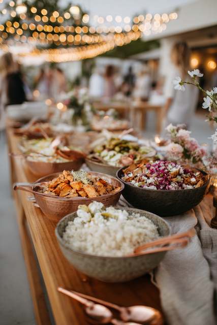 Build-Your-Own Bowl Station A variety of dishes in bowls, including rice and roasted vegetables, elegantly set on a wooden table under romantic string lights outdoors.