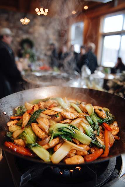 Build-Your-Own Stir Fry Station A sizzling stir fry with chicken, bok choy, and vegetables in a wok, set in a lively wedding reception with warm, cozy decor.