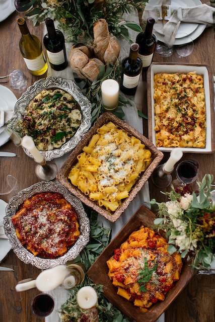 Family-Style Pasta Dishes Family-style pasta dishes elegantly arranged on a wooden table with wine bottles and bread, creating a cozy, communal dining setup.