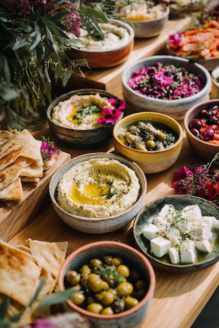 Mediterranean Mezze Spread A vibrant Mediterranean mezze spread featuring hummus, olives, feta, and pita, beautifully arranged with flowers for a wedding buffet.