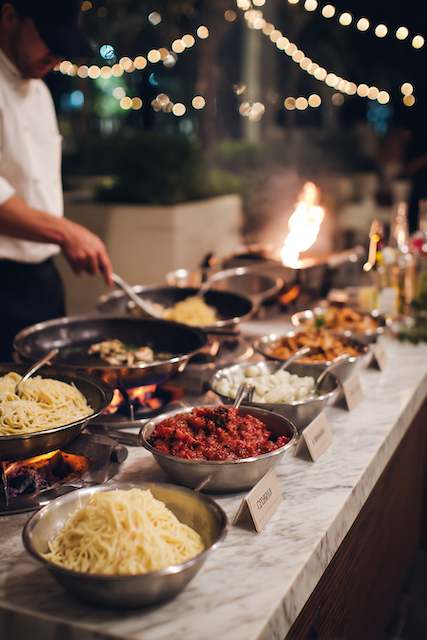 Pasta Station with Mix-and-Match Options A chef prepares pasta at a nighttime wedding pasta station, illuminated by string lights in an elegant outdoor setting