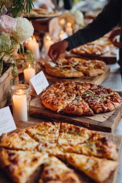Pizza Station A variety of freshly baked pizzas on wooden boards, surrounded by candles and flowers, creating a cozy and inviting atmosphere.