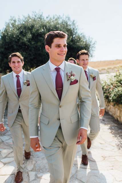 Sage Green & Burgundy groomsmens outfits Groom and groomsmen in sage green suits with burgundy accents, walking down a scenic outdoor path, showcasing a stylish wedding party
