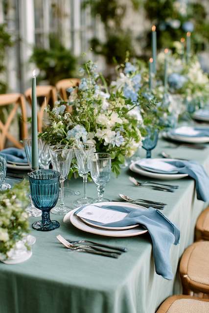 Sage Green & Dusty Blue wedding dinner table Elegant sage green wedding tablescape accented with dusty blue napkins, blue glass goblets, and lush floral centerpieces in white and soft blue tones