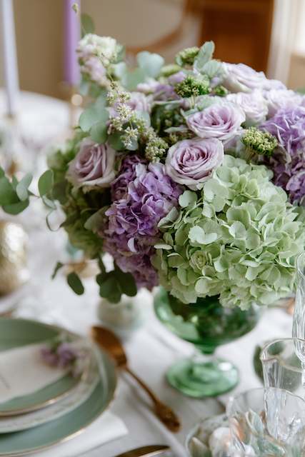 wedding centerpiece featuring a mix of lavender roses and green hydrangeas arranged in a vintage green glass vase, with soft lighting to highlight the delicate flowers Sage Green & Lilac floral centerpiece