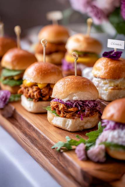 Slider Bar with Assorted Mini Sandwiches Assorted slider sandwiches on a wooden platter with vibrant garnishes, perfect for a festive and budget-friendly wedding buffet.