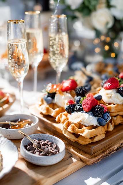 Sunday Brunch Reception Waffles topped with whipped cream and fresh berries, accompanied by glasses of champagne, creating an elegant brunch setting.