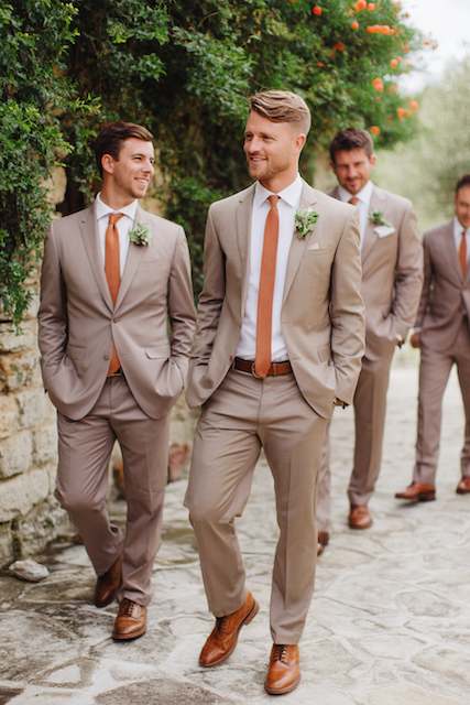 groomsmen wearing terracotta color ties Groomsmen wearing light tan suits with terracotta ties and brown shoes walking outdoors — perfect neutral attire for a sage green and terracotta wedding palette