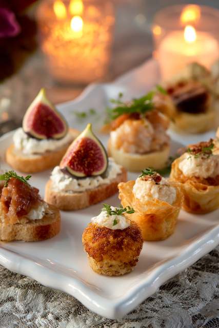 hors d'oeuvres for Appetizer-Only Reception An elegant selection of appetizers on a platter, featuring crostini with figs, shrimp bites, and cheese puffs, complemented by candlelit ambiance for a sophisticated wedding event.