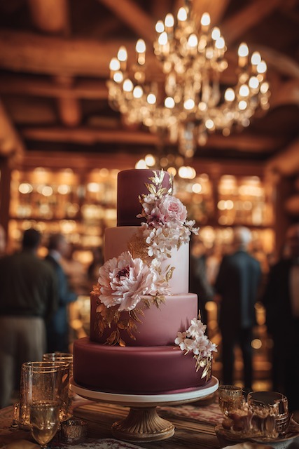 Burgundy + blush wedding cake Four tier burgundy and blush ombré wedding cake with gold leaf accents and cascading sugar flowers, exuding rich romantic elegance in a candlelit setting.
