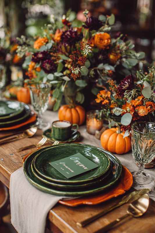 Burnt orange + deep green fall country wedding Fall wedding table setup featuring green plates, rustic wood decor, orange pumpkins, and vibrant floral centerpieces with deep purple, orange, and green accents, capturing a cozy autumn vibe