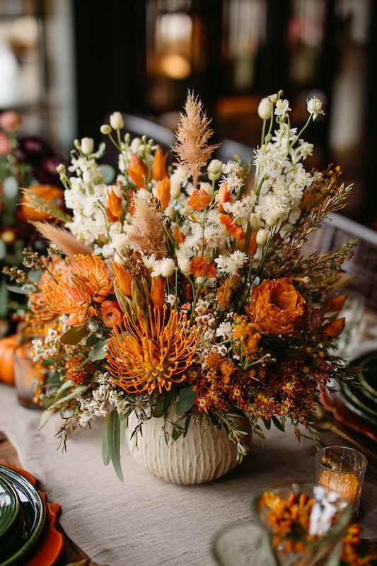 Dried flowers mixed with fresh blooms Large autumn floral arrangement with orange and white blooms, including protea, pampas grass, and seasonal foliage, arranged in a textured ceramic vase, creating a warm and inviting fall atmosphere