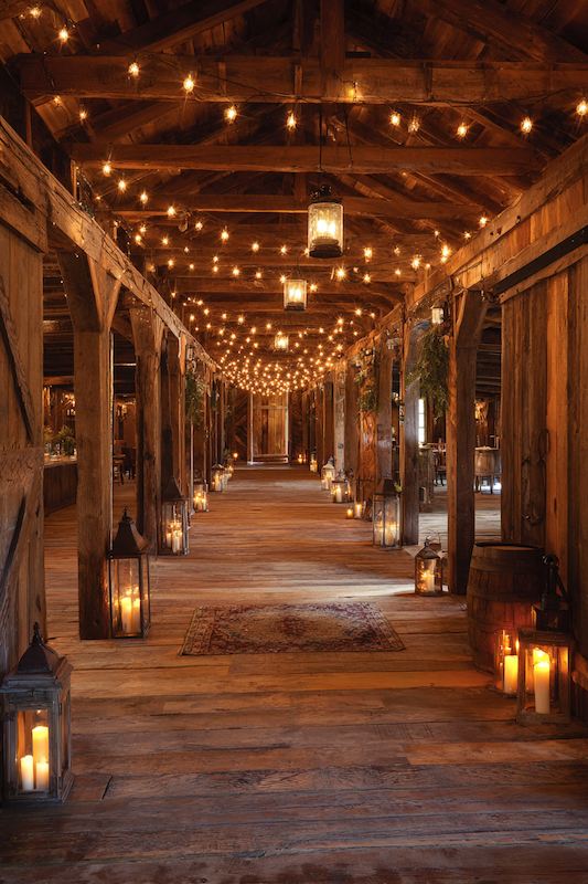 A rustic barn hallway lit with warm string lights and vintage lanterns, creating a romantic and magical atmosphere for a cowboy wedding