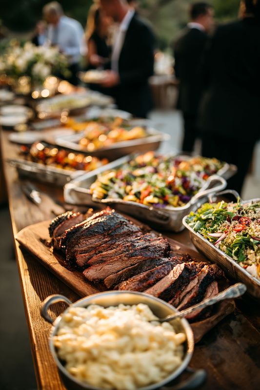 A beautifully arranged cowboy wedding buffet featuring roasted meats, vibrant salads, and a variety of sides served on rustic wooden tables