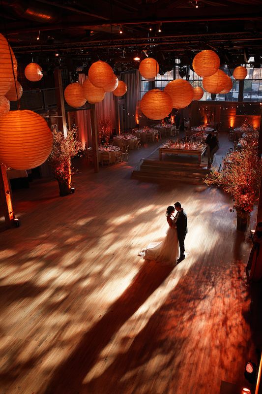 A bride and groom share a romantic first dance under glowing orange lanterns at an elegant wedding reception