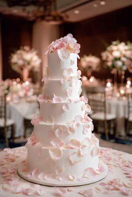 Scattered rose petals on icing wedding cake Five tier white wedding cake with soft pink rose petals on smooth icing, on a round table with romantic candlelit background.