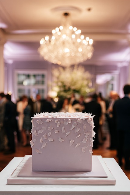 Single tier square design wedding cake Square wedding cake adorned with delicate white petal decorations, set against a luxurious chandelier-lit reception backdrop