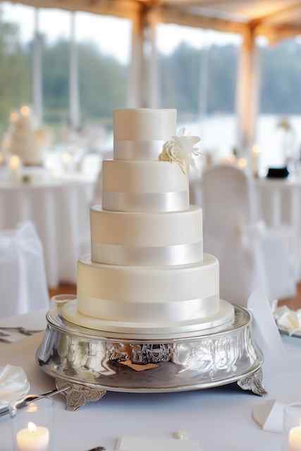 four tiered wedding cake with satin ribbons Five-tiered wedding cake adorned with satin ribbons and a single white flower, set on a silver pedestal with soft lighting in the background