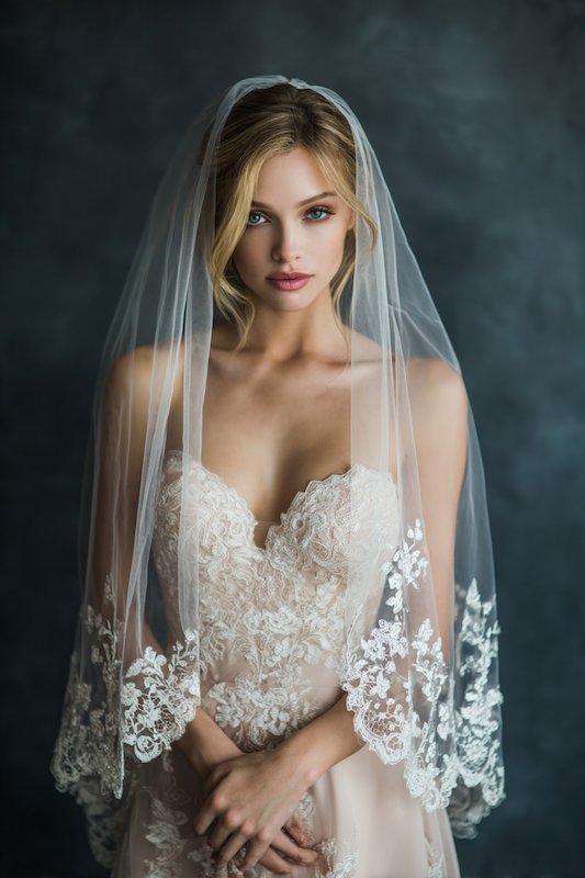 Fingertip Veil A bride wearing a beautifully detailed lace gown with an intricate floral design, paired with a long veil that cascades elegantly, creating a soft and romantic loo