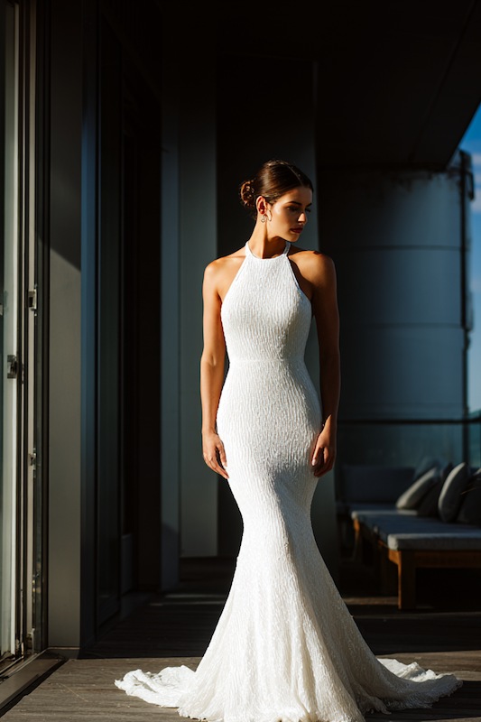 Halter mermaid wedding dress A bride in a halter-neck mermaid wedding gown with textured fabric, creating a sleek and modern silhouette