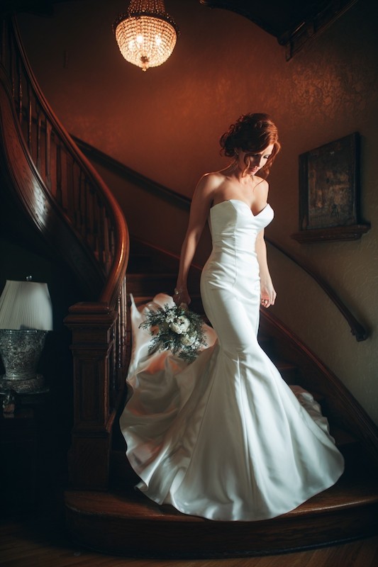 Movement restrictions of mermaid wedding dress A bride in a strapless mermaid wedding dress descending a staircase while holding a bouquet, with a dramatic train flowing behind her