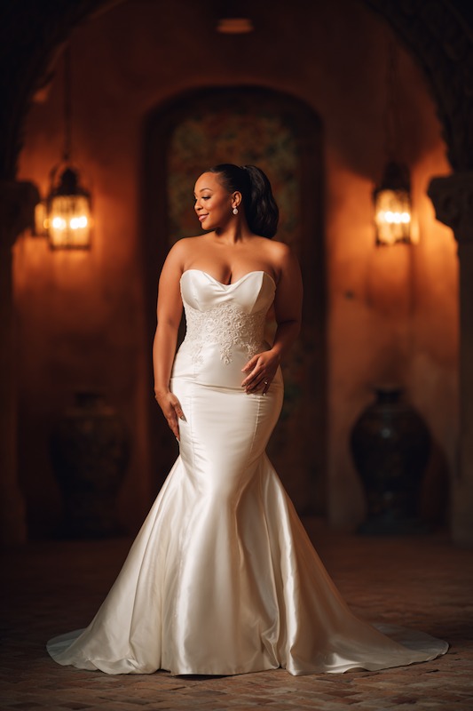 bride in mermaid wedding dress Curvy bride in a strapless mermaid wedding dress with floral detailing, standing gracefully with a serene expression in a softly lit, romantic setting