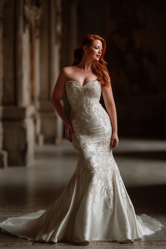 pear shaped bride in mermaid wedding dress Curvy bride in a strapless mermaid wedding dress with intricate lace detailing, posing gracefully in a grand, elegant space