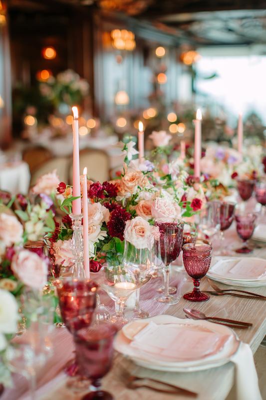 Wedding Reception Ideas in the form of an Elegant wedding reception table with pink taper candles, lush floral centerpieces of roses and greenery, and vintage-style glassware in shades of blush and berry.