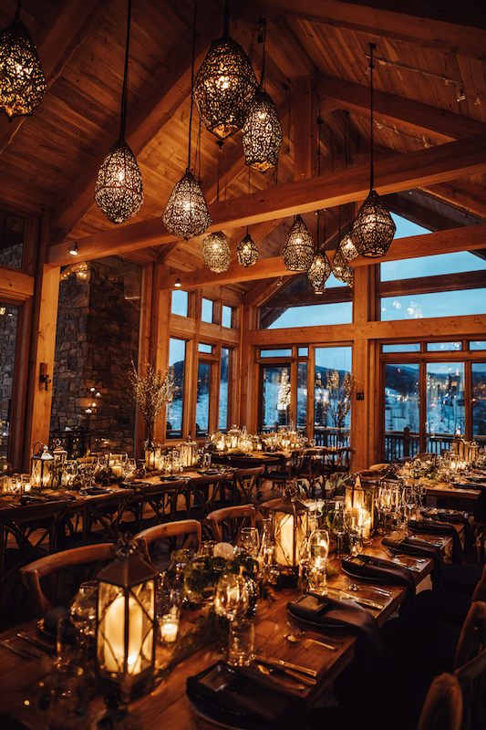Rustic winter wedding dinner setting with candlelight, wood beams, and elegant pendant lights overhead