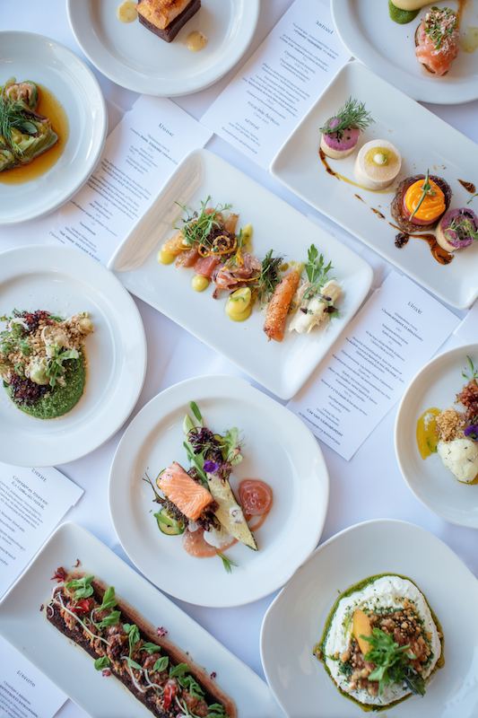 Wedding Tasting: What You Need to Know 3 Overhead view of assorted gourmet wedding tasting dishes on white plates, arranged with colorful garnishes and menus underneath