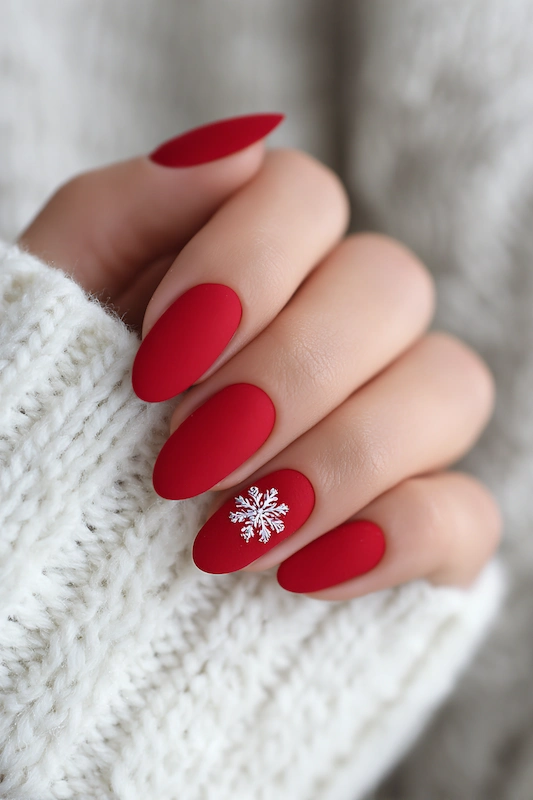 Close-up of a hand with matte red almond-shaped nails, featuring a white snowflake design on the ring finger, against a cozy white knit sweater Close-up of a hand with matte red almond-shaped nails, featuring a white snowflake design on the ring finger, against a cozy white knit sweater