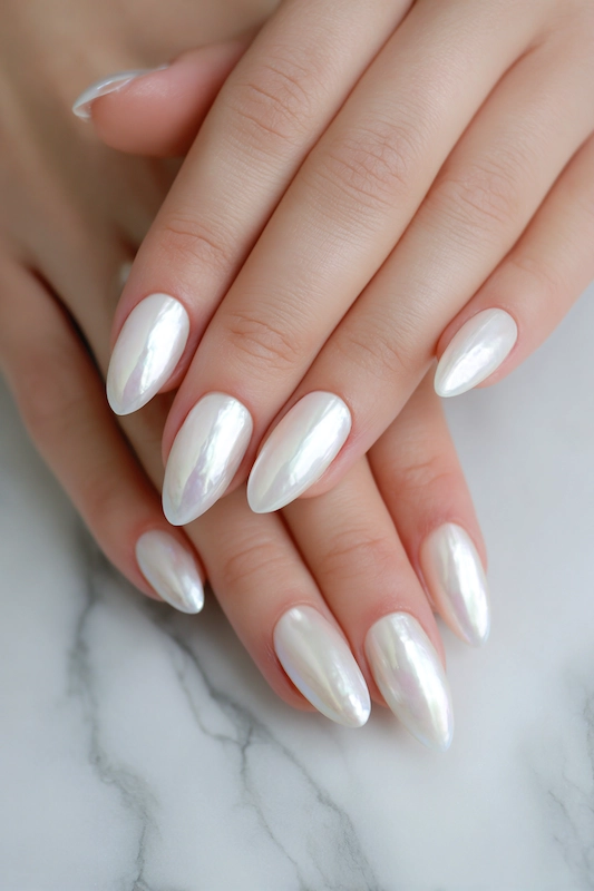 Close-up of hands with long, almond-shaped nails in a shiny, iridescent pearl white finish, resting on a white marble background Close-up of hands with long, almond-shaped nails in a shiny, iridescent pearl white finish, resting on a white marble background