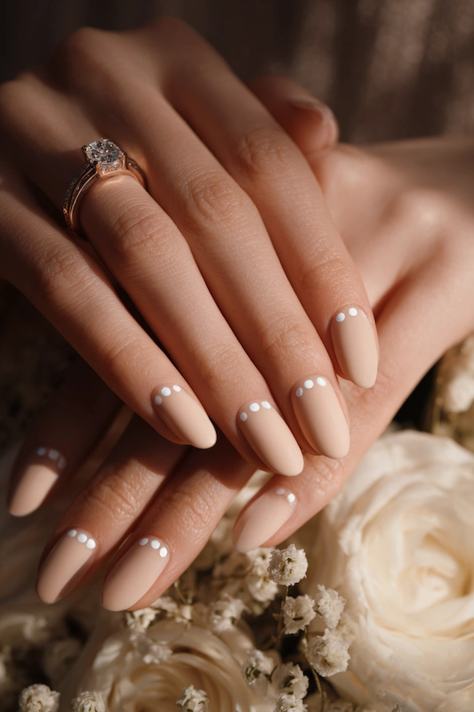 Hands with nude nails and three white dots near the base, resting on white roses. A diamond ring is on the ring finger Hands with nude nails and three white dots near the base, resting on white roses. A diamond ring is on the ring finger