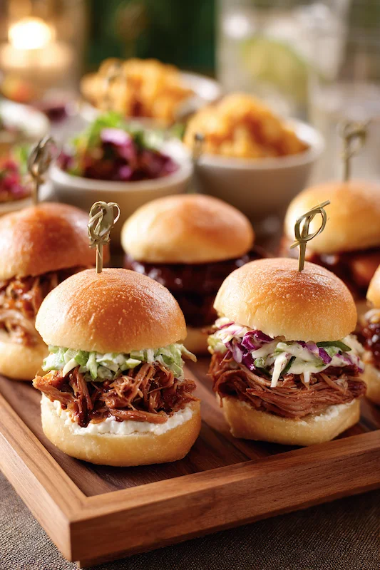25 Wedding BBQ Buffet Ideas That Instantly Upgrade Your Reception 7 Pulled pork sliders with coleslaw on soft buns, served on a wooden tray with side dishes in the background