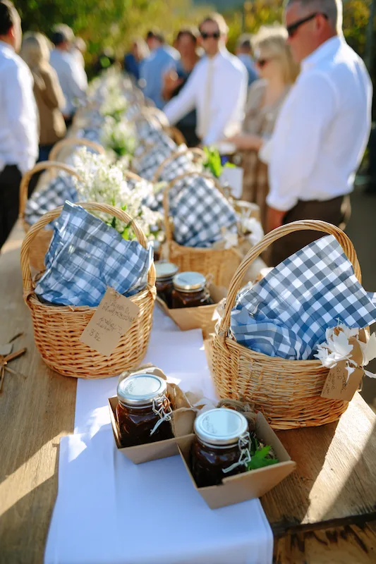 25 Wedding BBQ Buffet Ideas That Instantly Upgrade Your Reception 13 Picnic basket wedding buffet with blue gingham napkins, mini jars of BBQ sauce, and rustic wooden table outdoors