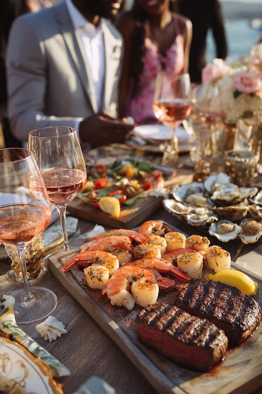 25 Wedding BBQ Buffet Ideas That Instantly Upgrade Your Reception 3 Grilled shrimp, scallops, and steaks served with lemon wedges, fresh vegetables, and rose wine glasses at a festive outdoor gathering