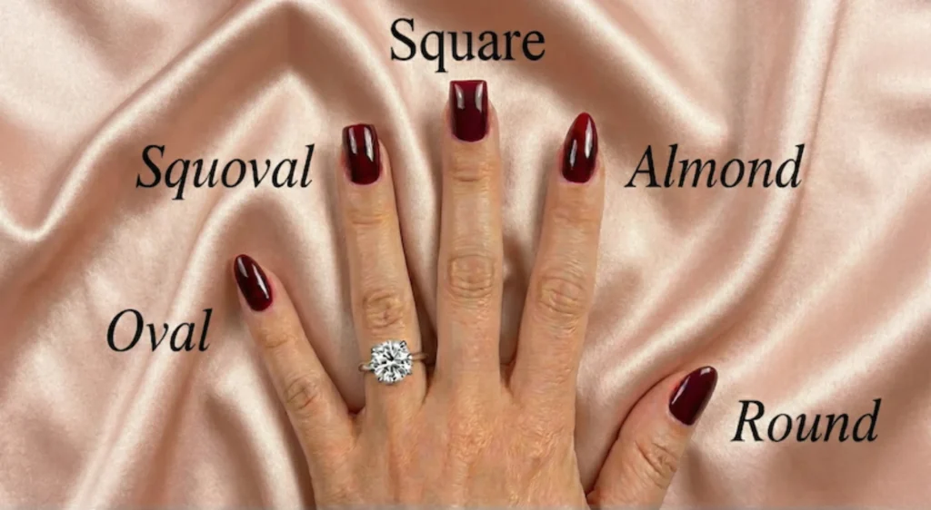 Beyond the Almond: The 2026 Engagement Nail Trends Defining "Intentional Glamour" 7 Hand with burgundy manicure showing square, squoval, almond, oval, and round nail shapes with diamond engagement ring on satin background