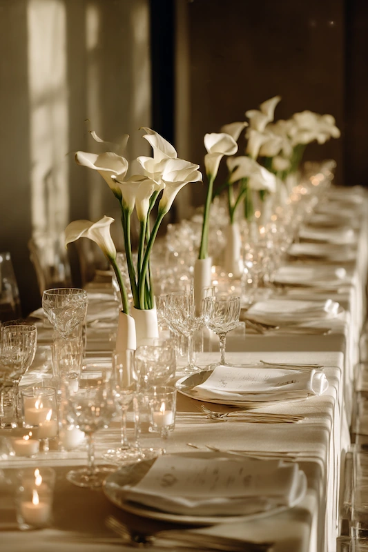 Modern Wedding Reception Decor Trends Couples Are Choosing in 2026 6 Elegant wedding dinner table with white calla lily centerpieces, crystal glassware, candles, and ivory linens in warm light