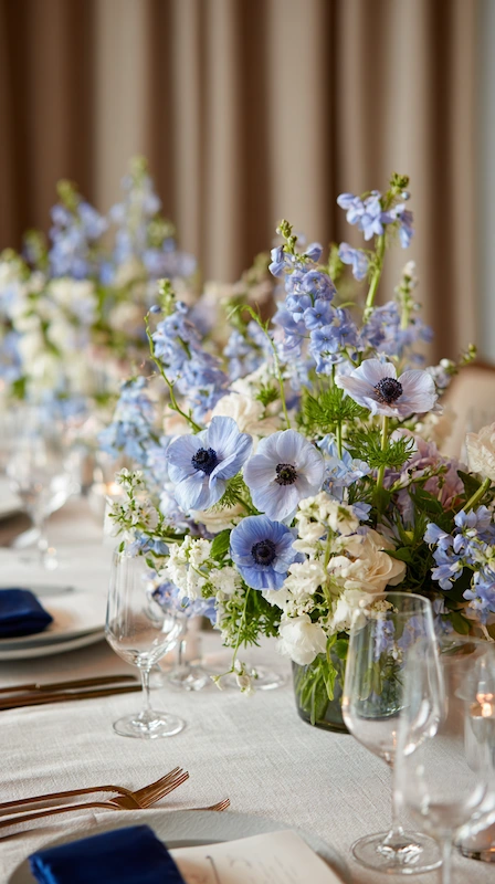 35 Spring Wedding Centerpieces With Flower Pairings Brides Can Actually Use 8 Whimsical wedding table with blue anemones and delphinium in small vases, soft greenery, candles, and airy elegant place settings