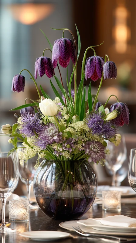 35 Spring Wedding Centerpieces With Flower Pairings Brides Can Actually Use 20 Elegant wedding centerpiece with purple fritillaria, white tulips, and textured blooms arranged in a reflective glass vase