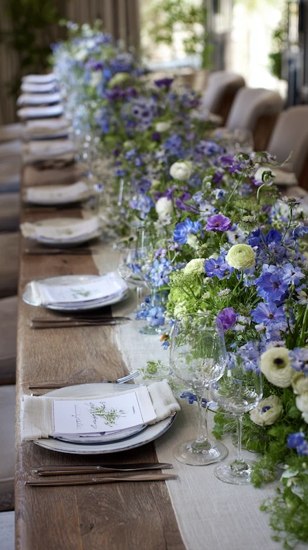 35 Spring Wedding Centerpieces With Flower Pairings Brides Can Actually Use 25 Long wedding reception table with blue and green floral garland, soft garden blooms, and elegant neutral place settings