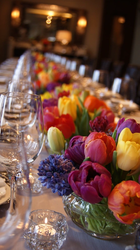 35 Spring Wedding Centerpieces With Flower Pairings Brides Can Actually Use 11 Long wedding table with vibrant tulip centerpieces in low bowls, candlelight glow, crystal glassware, and elegant evening ambiance