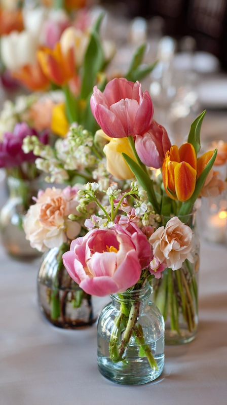35 Spring Wedding Centerpieces With Flower Pairings Brides Can Actually Use 2 Spring wedding centerpiece with pink and orange tulips, ranunculus, and sweet pea arranged in small glass bud vases