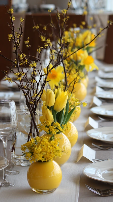 35 Spring Wedding Centerpieces With Flower Pairings Brides Can Actually Use 6 Sunny yellow wedding table with tulips and forsythia branches in round vases, white plates, place cards, and airy spring styling