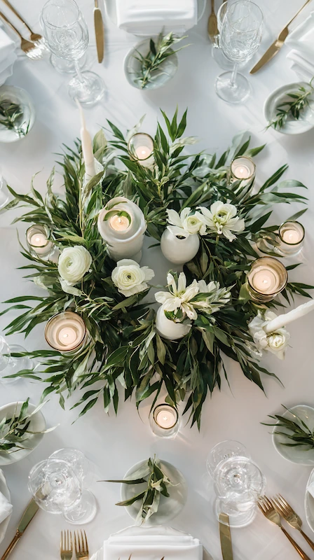 Wedding Centerpiece Ideas for Round Tables (3-2-1 Formula) 8 Overhead wedding table with greenery wreath centerpiece, white florals, pillar candles, gold flatware, and elegant place settings