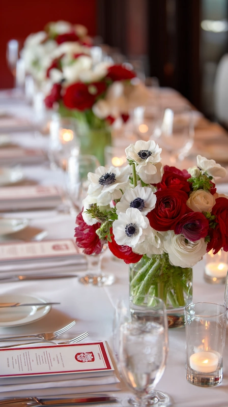 Red ranunculus and white anemone wedding centerpieces with candlelight, long reception table, crisp linens, and elegant place settings