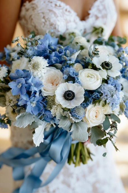 Dusty Blue Wedding Decor: Florals, Table Settings and Reception Styling 2 Close-up of a dusty blue bridal bouquet with white roses, anemones, delphiniums, eucalyptus, and a blue silk ribbon.